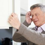 Older man with dementia standing in front of a cabinet looking confused