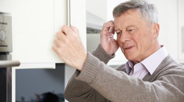 Older man with dementia standing in front of a cabinet looking confused