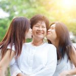 Older Asian woman being kissed on the check by her two daughters.