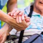Elderly woman in wheelchair holding hand of caregiver
