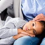 Latina girl with her head on her mom's lap, mother is stroking her hair